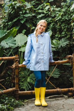 beautiful young woman in blue raincoat and yellow rubber boots in rainforest clipart