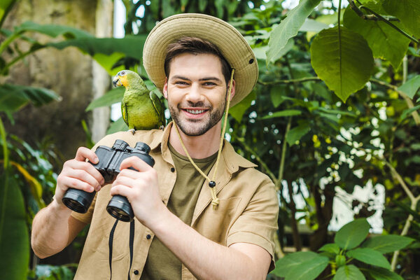 happy young man with parrot on shoulder and binoculars looking at camera
