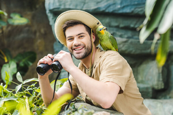 handsome young man with parrot on shoulder and binoculars looking at camera