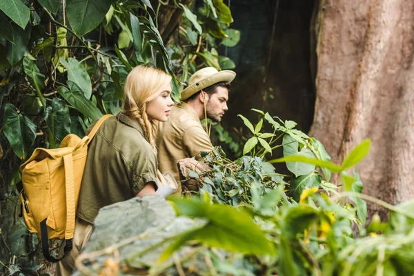 active young couple in safari suits hiking in jungle and looking somewhere impressed