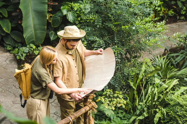 beautiful young couple in safari suits with map in jungle