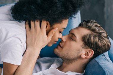 Genç çok ırklı çift kanepede yatan süre öpüşme