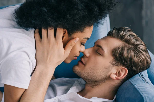 Young Multiracial Couple Kissing While Lying Sofa — Stock Photo, Image