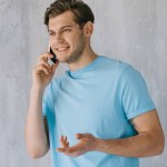 Young man talking on the phone by gray wall