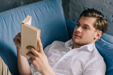 Genç adam evde kitap ile kanepede rahatlatıcı