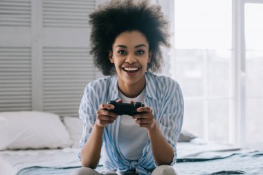 Afrikalı-Amerikalı kadın yatakta otururken video oyun oynarken joystick ile