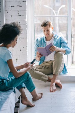 Afrikalı-Amerikalı kadın pencere kitap okuma adam telefonda müzik dinlemek