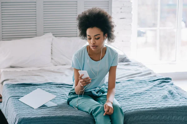 African American Kobieta Siedzi Łóżku Słuchanie Muzyki Telefon — Zdjęcie stockowe