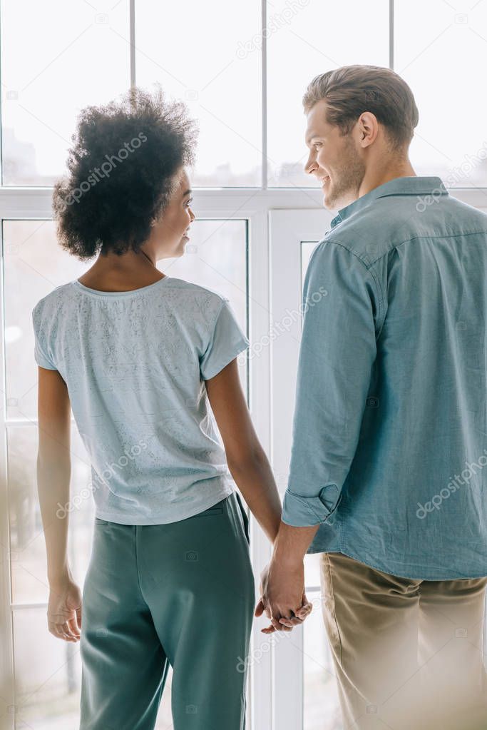Loving couple holding hands by window in room