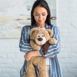 Portrait of smiling attractive woman with teddy bear in hands at home