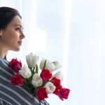 Boční pohled krásná zamyšlená žena s kyticí tulipánů doma