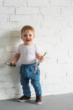 mutlu küçük oğlu beyaz tuğla duvarın ayakta oyuncaklar ile