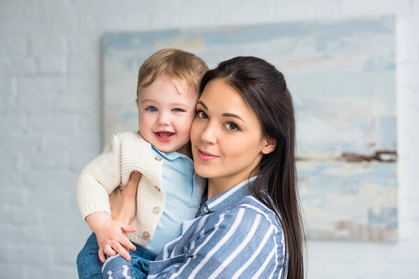portrait of young mother holding cheerful adorable baby boy in hands at home