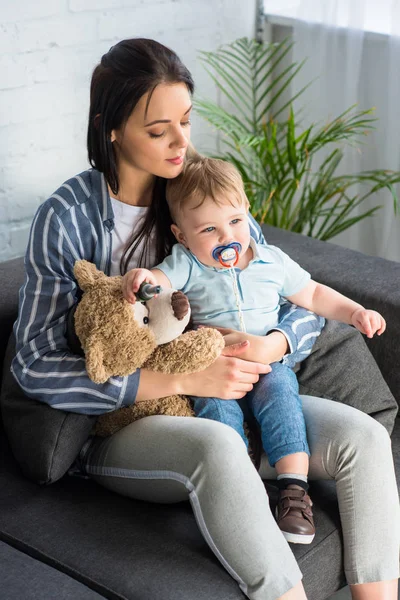 Madre Joven Pequeño Bebé Con Chupete Osito Peluche Sentado Sofá — Foto de Stock