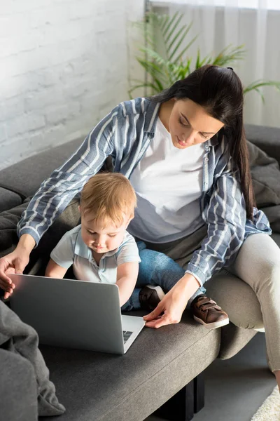 ノート パソコンと自宅のソファの上のかわいい赤ちゃんと母 仕事と生活バランスの概念 — ストック写真
