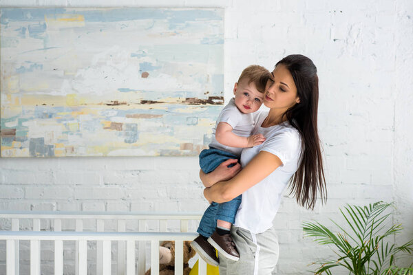young mother holding cute baby boy in hands at home