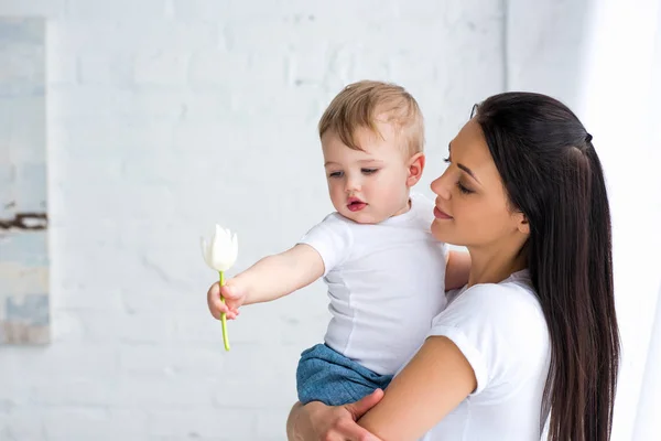 Madre Joven Sosteniendo Lindo Bebé Con Flor Tulipán Mano Casa — Foto de Stock