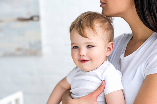 partial view of mother with cute little baby in hands at home