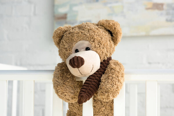 close up view of teddy bear hanging on white wooden baby crib in room
