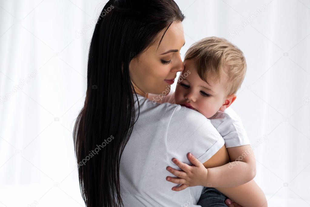 smiling tender mother holding cute baby boy in hands at home