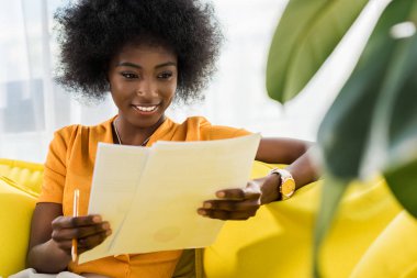 kağıtları evde kanepenin üzerinde çalışan uzak ile gülümseyen Afrikalı-Amerikalı kadın portresi