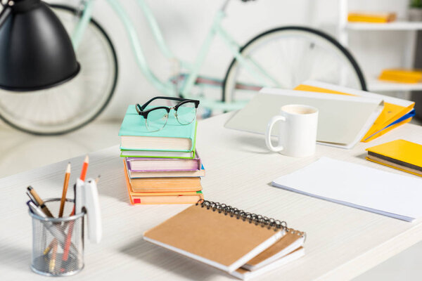 закрыть обзор груды книг, ноутбуков, папок, чашки кофе и очков на рабочем месте в домашнем офисе
