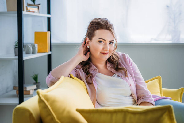 portrait of attractive woman sitting on sofa and looking at camera at home