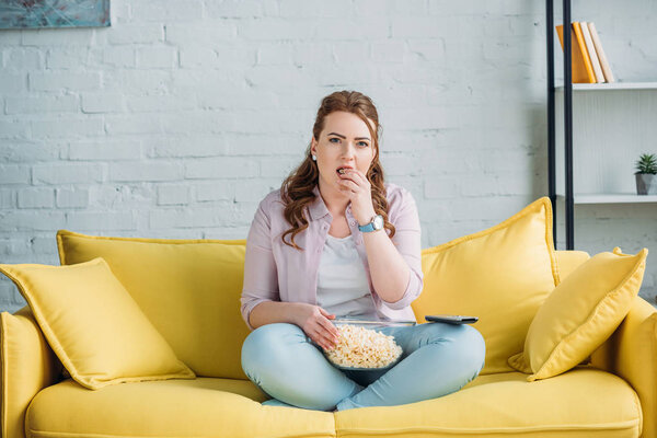 красивая женщина смотрит кино и ест попкорн дома
