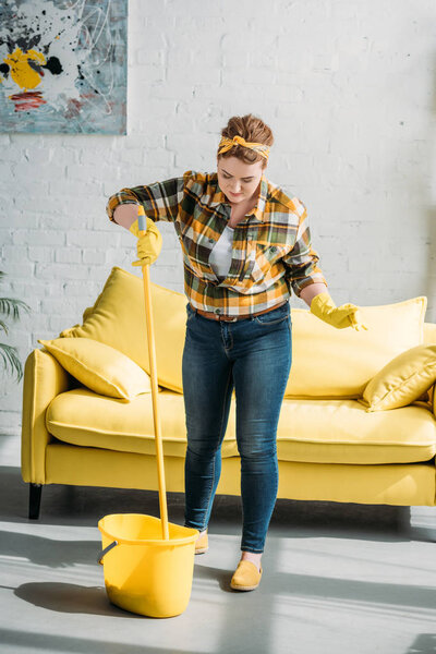beautiful woman putting mop into bucket with water at home