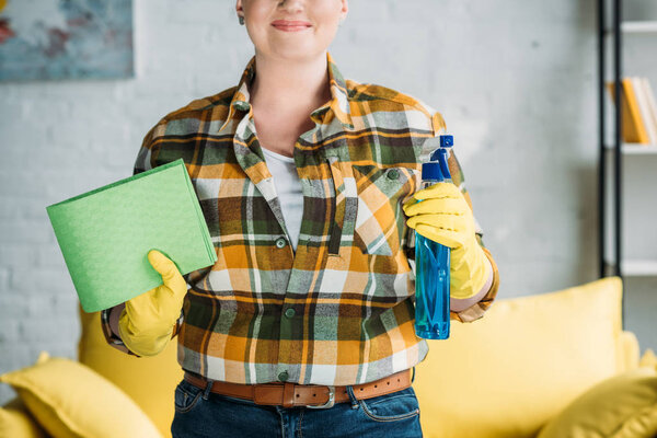 cropped image of woman holding rag and spray bottle for cleaning at home