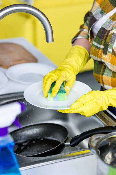 cropped image of woman washing plate with washing sponge in kitchen