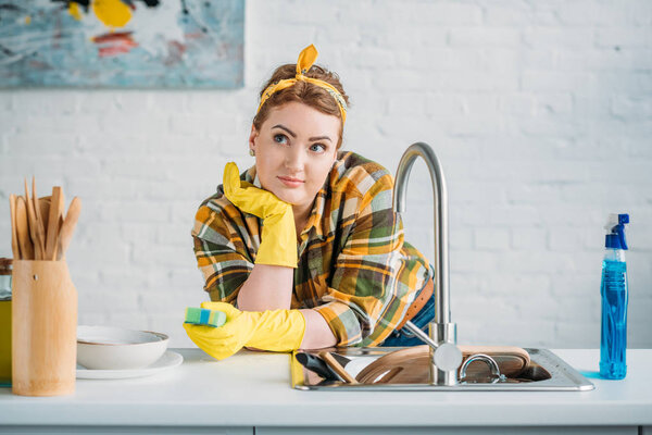 beautiful woman leaning on kitchen counter and holding washing sponge