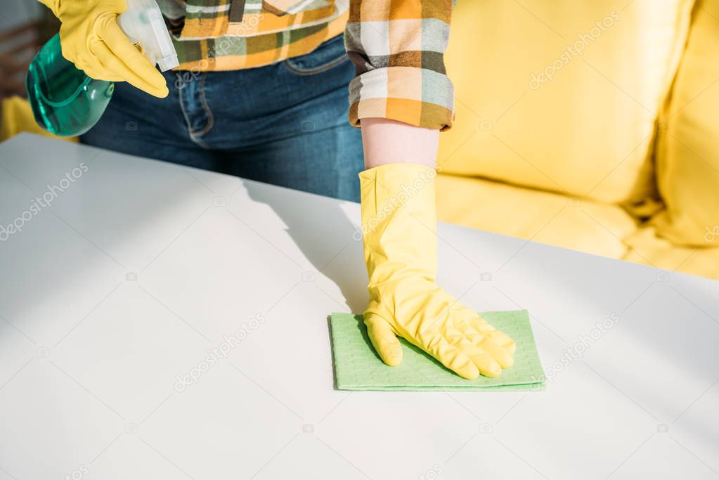 cropped image of woman cleaning table with spray bottle and rag at home