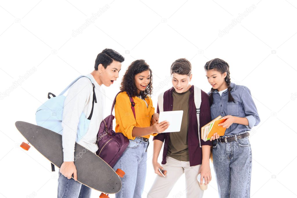 shocked multiracial students with backpacks and longboard using tablet together isolated on white