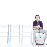 Aburrido adolescente estudiante escuchar música mientras sentado en silla aislado en blanco