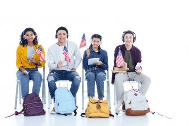 group of teen students in headphones with usa flags sitting on chairs isolated on white clipart