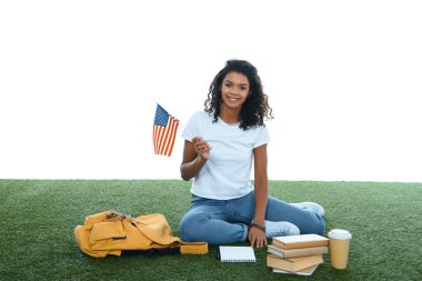 ABD bayrağı üzerinde beyaz izole çimenlerin üzerinde oturan genç Afro-Amerikan öğrenci kızla