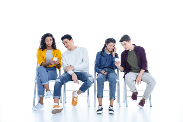 group of teen students using smartphones on chairs isolated on white