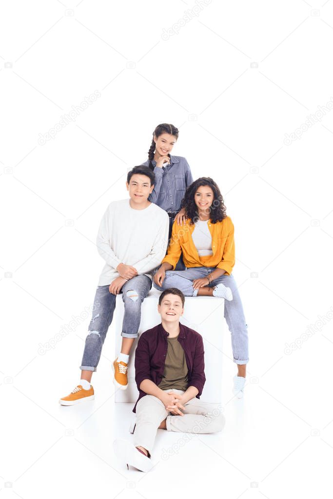 group of teen students sitting on white cube isolated on white