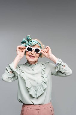 smiling senior woman in stylish headband and sunglasses isolated on grey clipart