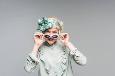 beautiful senior woman in stylish vintage clothes and sunglasses isolated on grey