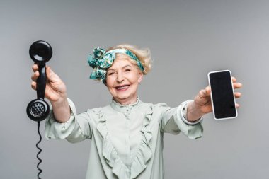 smiling senior woman with vintage phone and smartphone in hands isolated on grey clipart