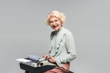 happy senior woman using typewriter on grey clipart