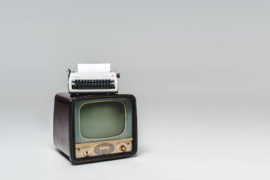 vintage tv with typewriter on top on grey surface clipart