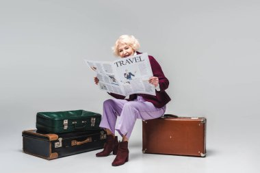 Vintage çanta üzerinde oturan ve seyahat gazetede Grey güzel kadın kıdemli