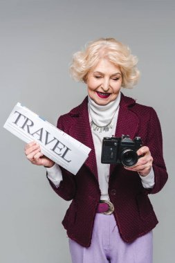 beautiful senior woman with travel newspaper and film camera isolated on grey clipart
