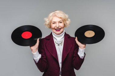 Vinil diskler üzerinde gri arka plan izole tutan mutlu şık üst düzey kadın 