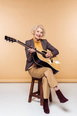 sandalyede oturan ve akustik gitar çalmaya şık kadın kıdemli gülümseyen 