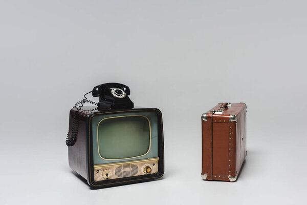 Vintage tv with rotary phone and suitcase on grey
