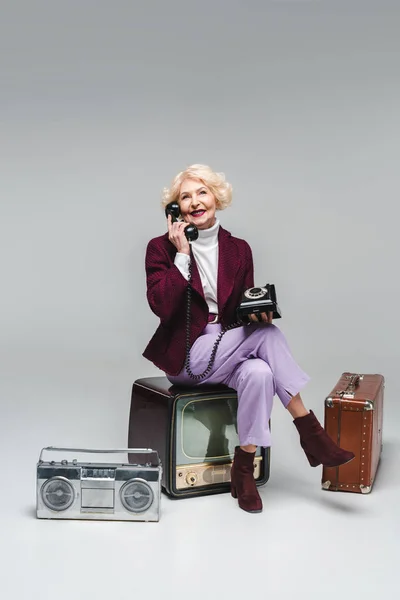 Schöne Seniorin Telefoniert Während Sie Vintage Fernseher Auf Grau Sitzt — Stockfoto
